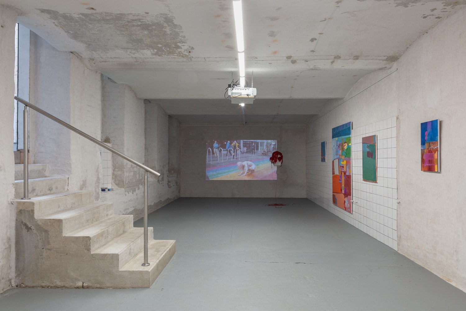 Installation view, What Remains, ArtLit Vienna, 2026: the basement space with the video projection by Diana Burkot and paintings by Olivia Kaiser